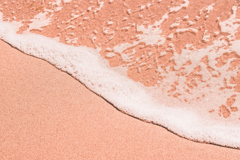 Gros plan sur une plage avec de l’écume qui arrive sur le sable qui est de couleur Peach Fuzz.